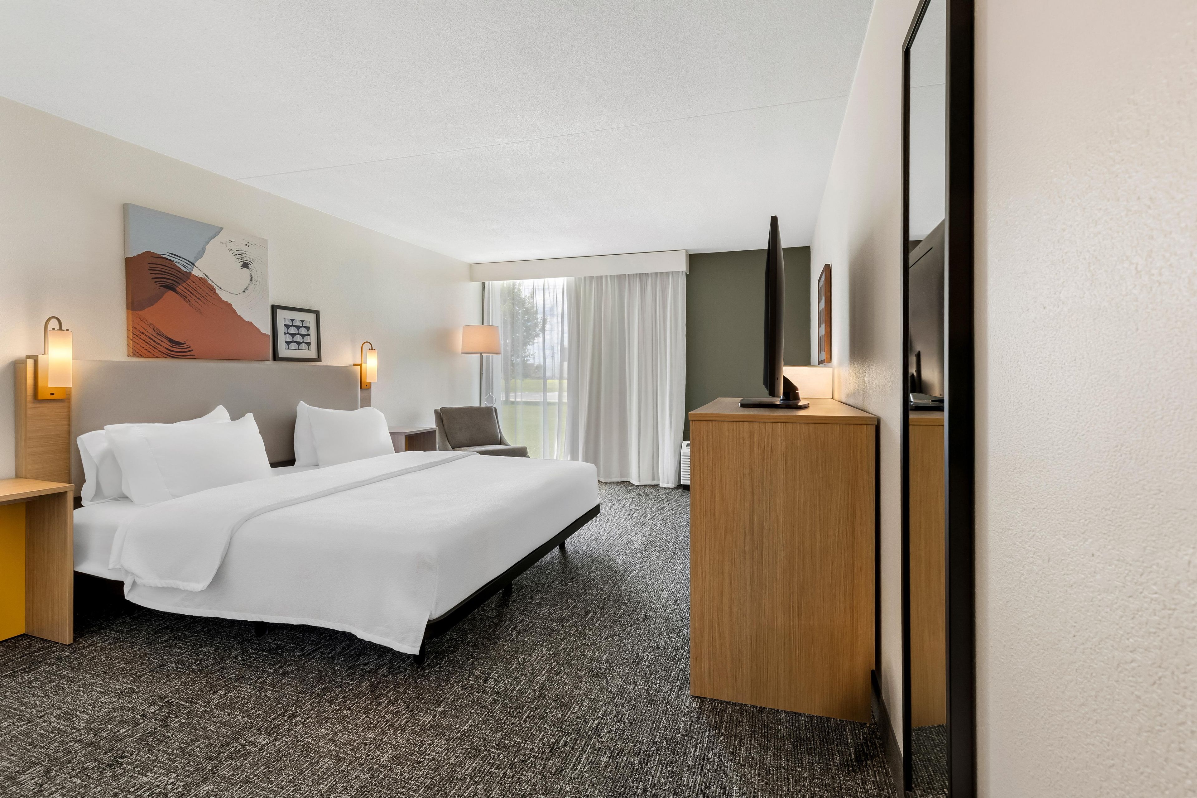 A hotel room with a large bed, a desk, a television, and artwork on the wall.