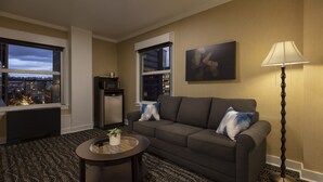A modern living room with a grey sofa, a round coffee table with a plant, a floor lamp, and a city view through large windows.