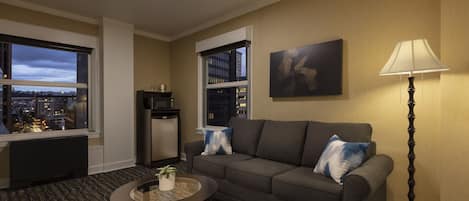 A modern living room with a grey sofa, a round coffee table with a plant, a floor lamp, and a city view through large windows.