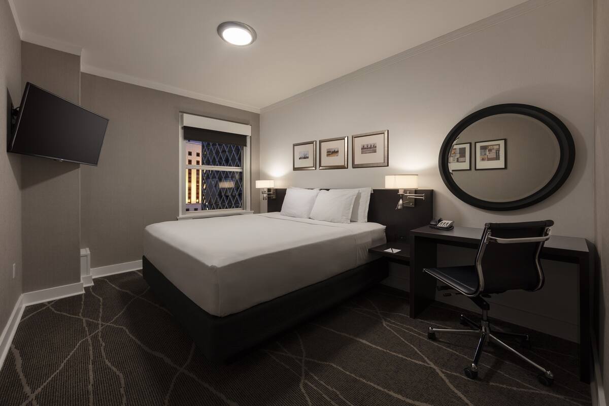 A hotel room with a large bed, a desk with a chair, a flat-screen TV mounted on the wall, and framed pictures on the wall.