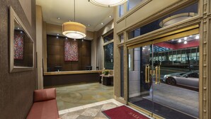 A hotel lobby with a reception desk, seating area, and a large glass door leading outside.