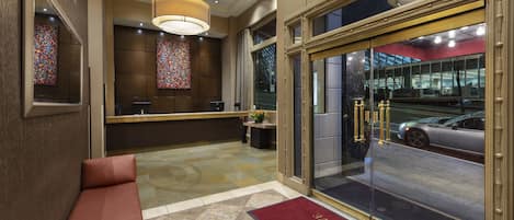 A hotel lobby with a reception desk, seating area, and a large glass door leading outside.