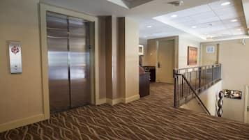 A hotel lobby with a carpeted floor, an elevator, a reception desk, and a staircase with a railing.