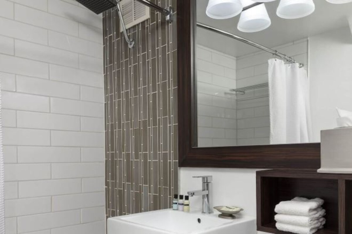 A modern bathroom with a white sink, a large mirror, and a shower with a bamboo-like wall.