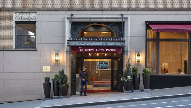 The Executive Hotel Pacific entrance with a brick facade, a red awning, and potted plants.
