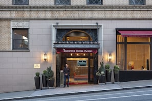 Executive Hotel Pacific -hotellin sisäänkäynti, jossa on tiiliverhous, punainen markiisi ja ruukkukasveja.