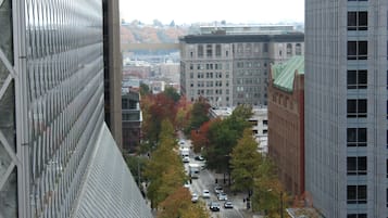 A city street with tall buildings, a mix of trees, and parked cars.