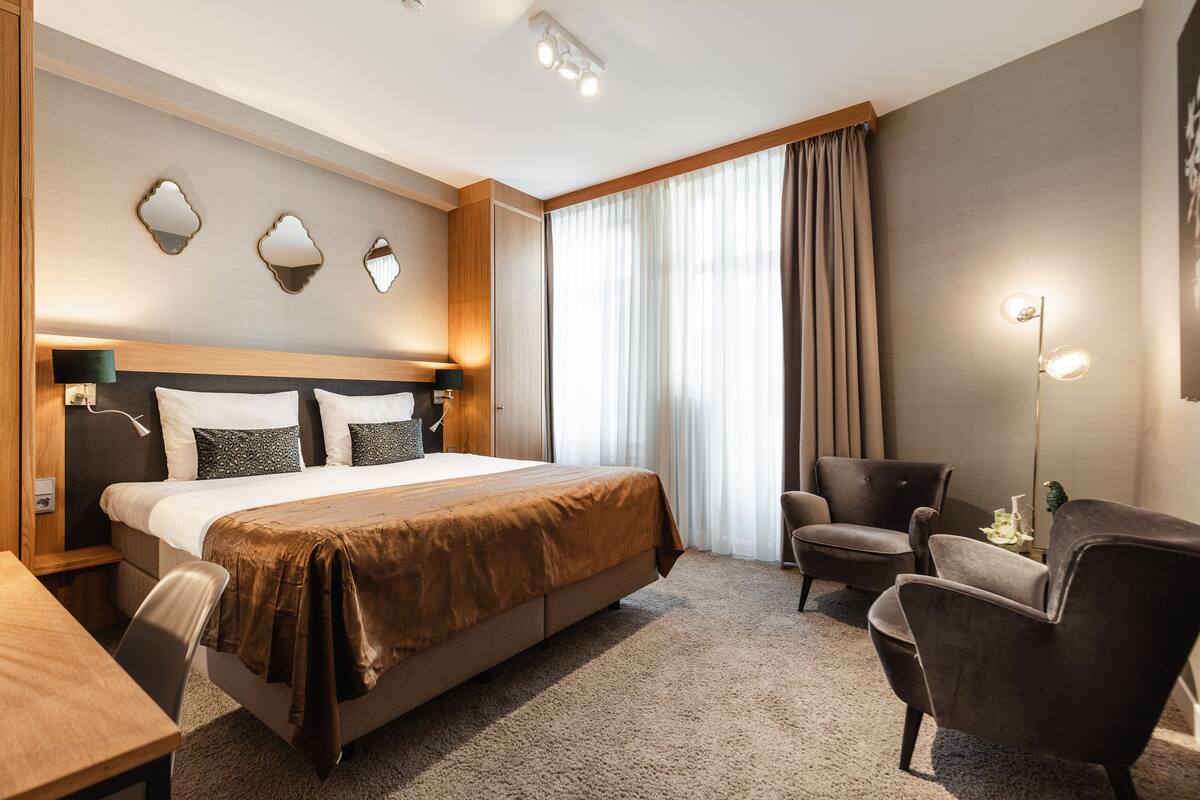 A hotel room with a large bed, two armchairs, a desk, and a nightstand.