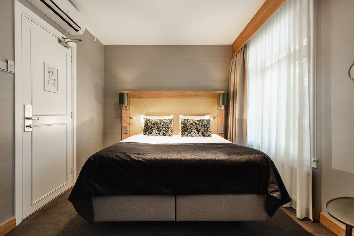 A hotel room with a bed, a door, and a window with curtains.