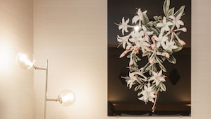 A room with two grey armchairs, a small round table with a vase of white flowers, and a floor lamp with three lights. - The Delphi - Amsterdam Townhouse (Amsterdam)