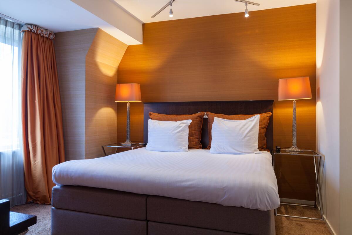 A modern hotel room with a large bed, two bedside lamps, and a wooden headboard.