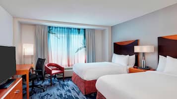 Een hotelkamer met twee bedden, een bureau met stoel, een televisie en een raam met gordijnen.