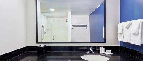 A modern bathroom with a large mirror, black countertop, white sink, and a glass shower enclosure.