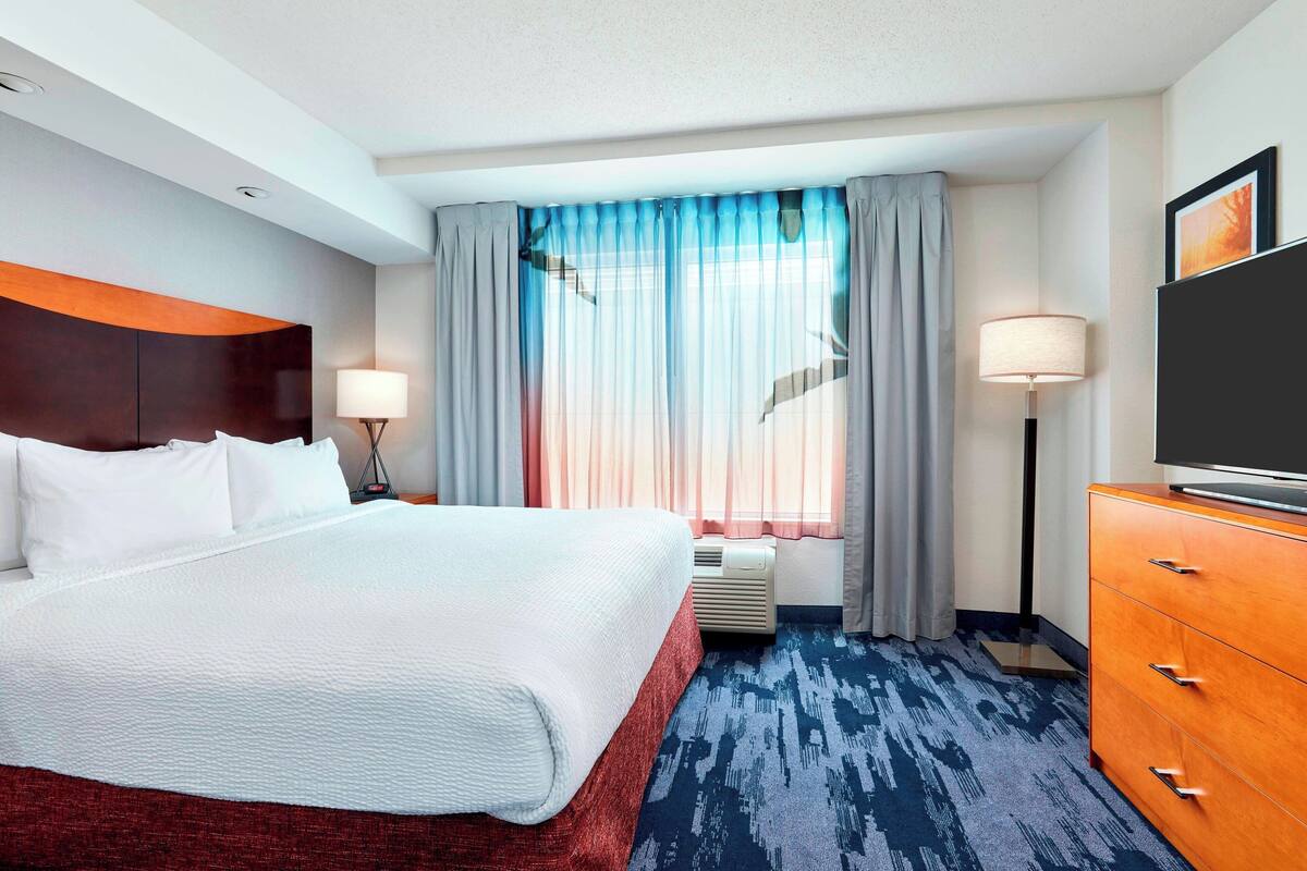 A hotel room with a large bed, a dresser, a TV, and a window with curtains.