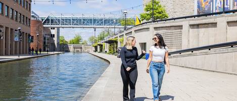 Two people walking along a waterfront promenade with a bridge in the background.