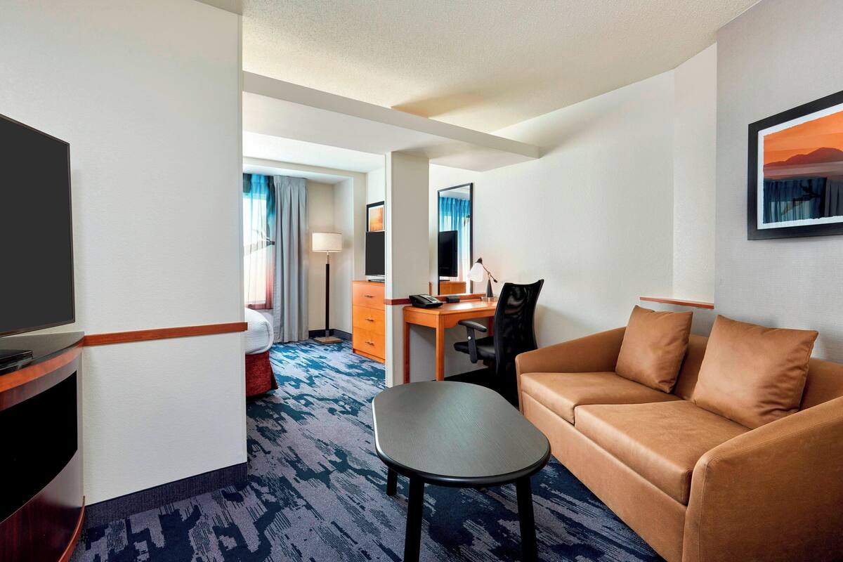 A hotel room with a sofa, a desk, a chair, a TV, and a bed.