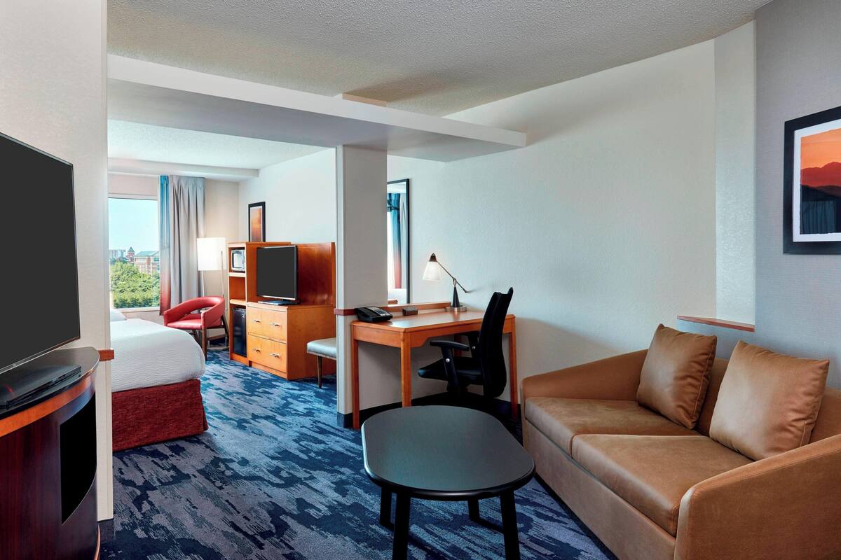 A hotel room with a bed, a desk, a chair, a sofa, and a TV.
