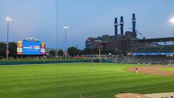 A baseball stadium with a large scoreboard, a field, and a brick building with chimneys in the background.