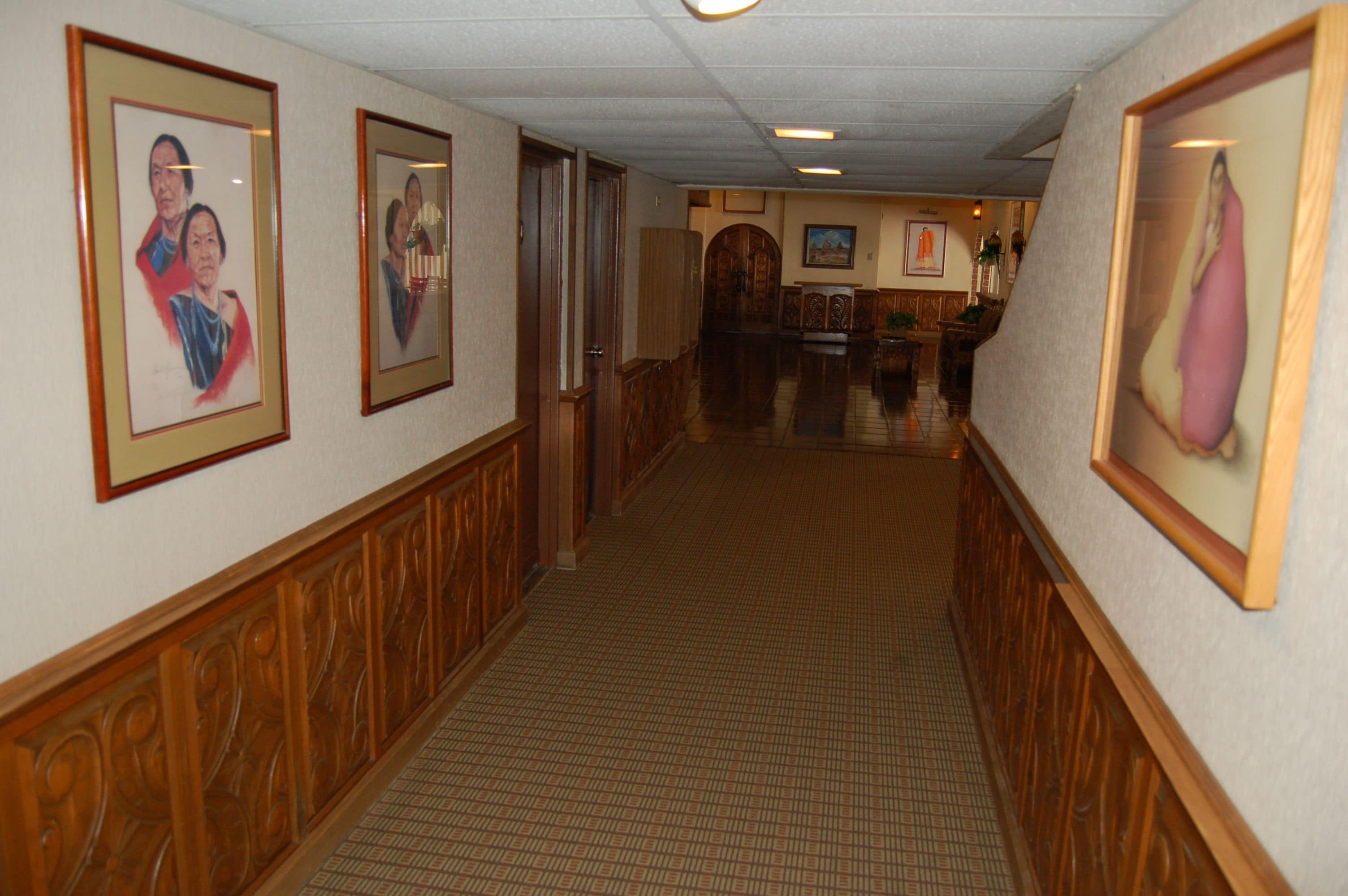 A hallway with framed portraits on the walls, wooden paneling, and a tiled floor.