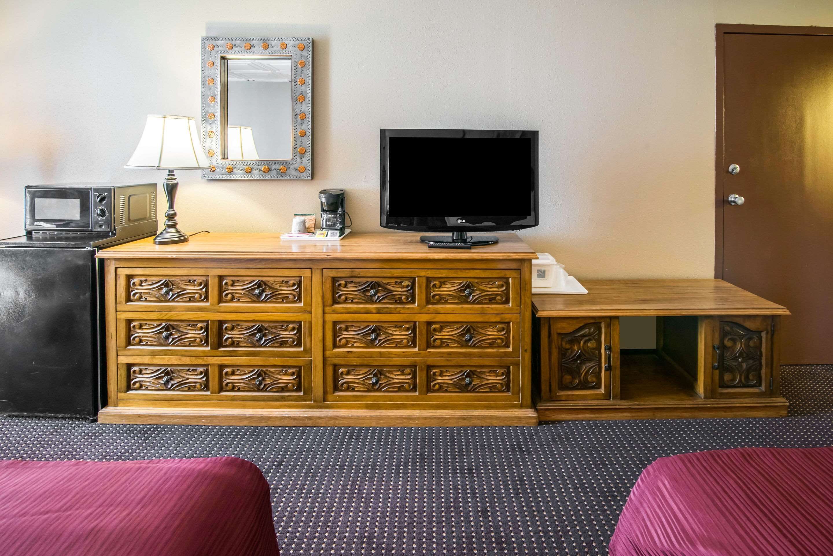 Una habitación de hotel con un armario de madera, un televisor, un microondas y una lámpara.