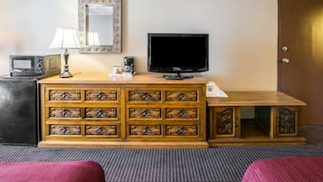 Una habitación de hotel con un armario de madera, un televisor, un microondas y una lámpara.