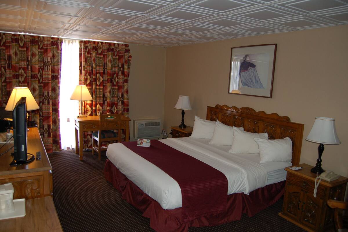 A hotel room with a large bed, two bedside tables with lamps, a desk with a computer, and a painting on the wall.