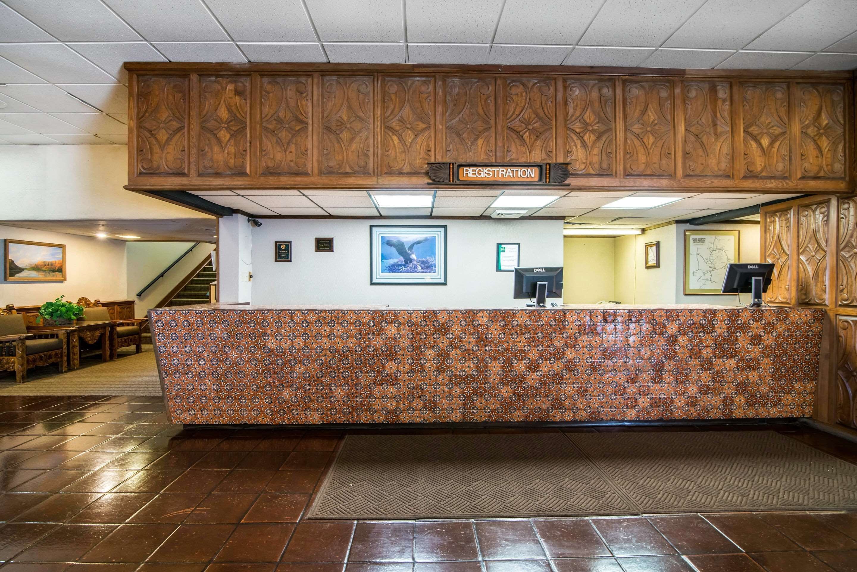 Un área de recepción con un mostrador de registro, un muro con diseño y una escalera al fondo.