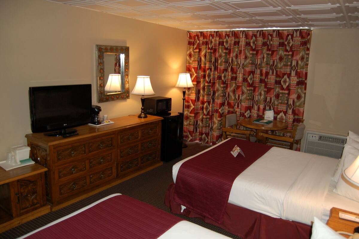 A hotel room with two beds, a TV, a dresser, lamps, and a patterned curtain.
