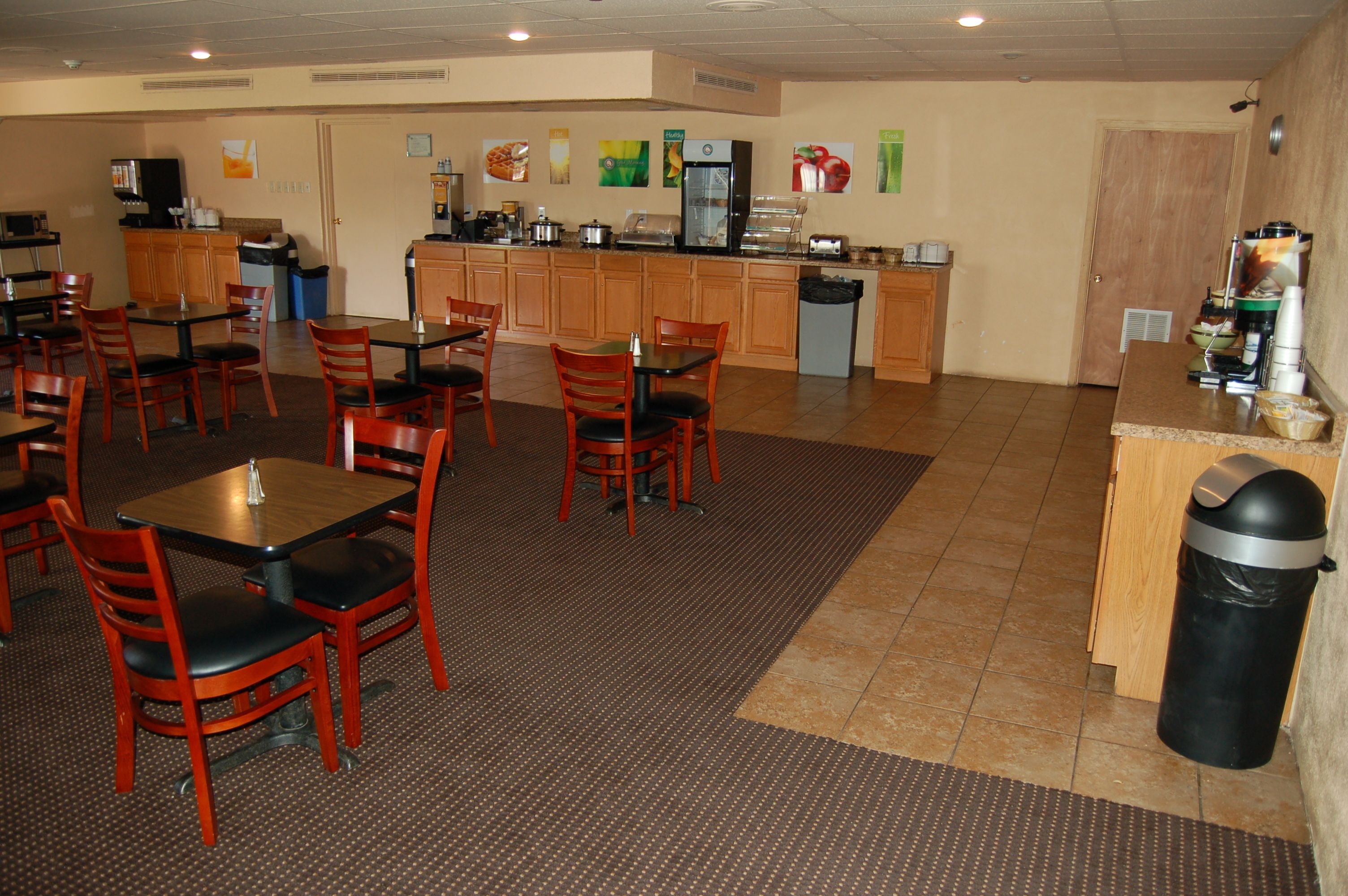 A restaurant with wooden tables and chairs, a kitchen area with appliances, and a trash can.
