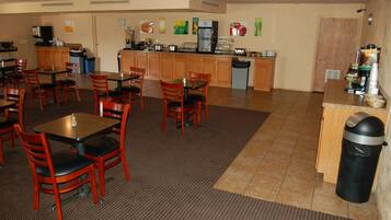 A restaurant with wooden tables and chairs, a kitchen area with appliances, and a trash can.