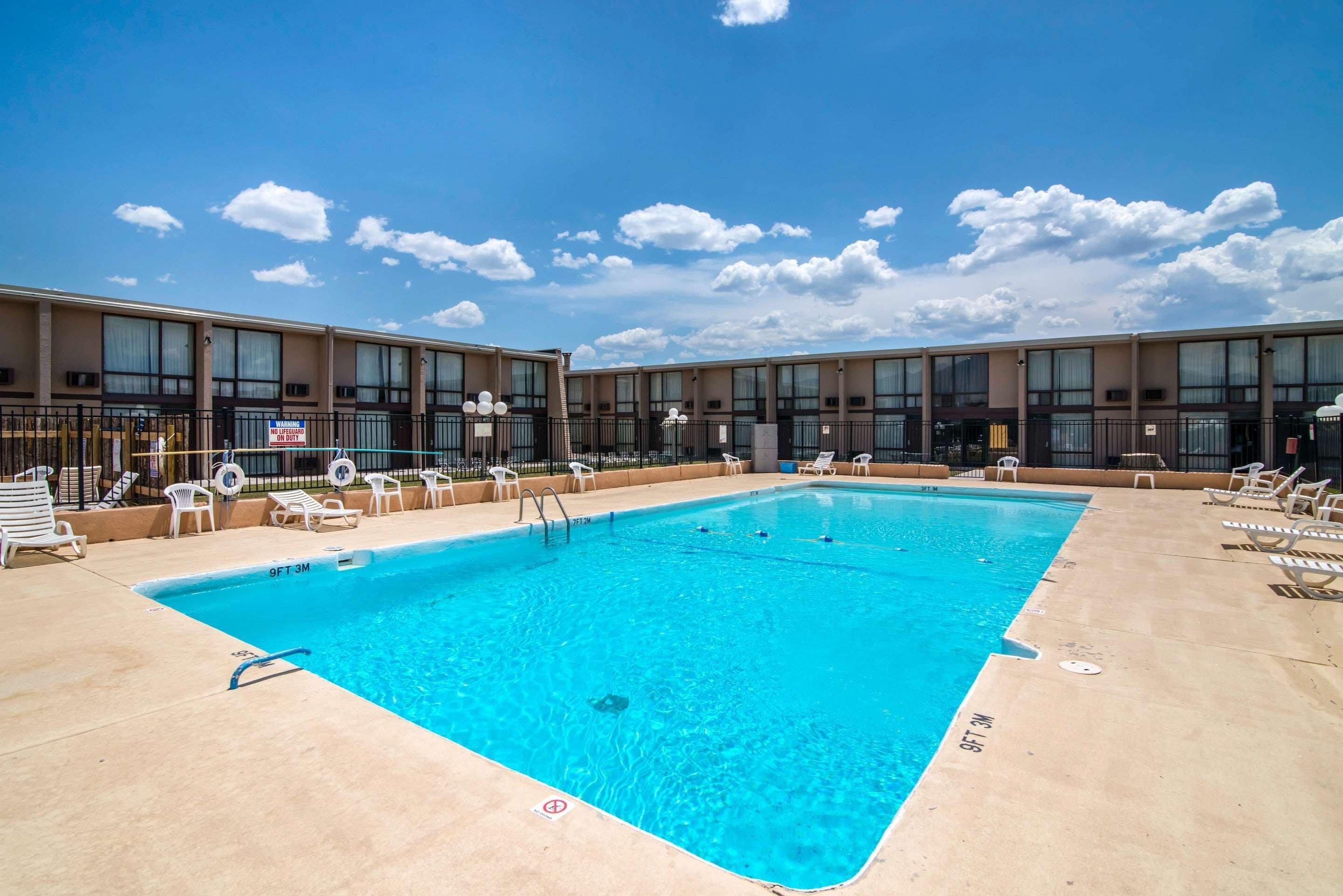 Ein rechteckiger Swimmingpool mit klarem, blauem Wasser, umgeben von Liegestühlen und einem Gebäude mit großen Fenstern.