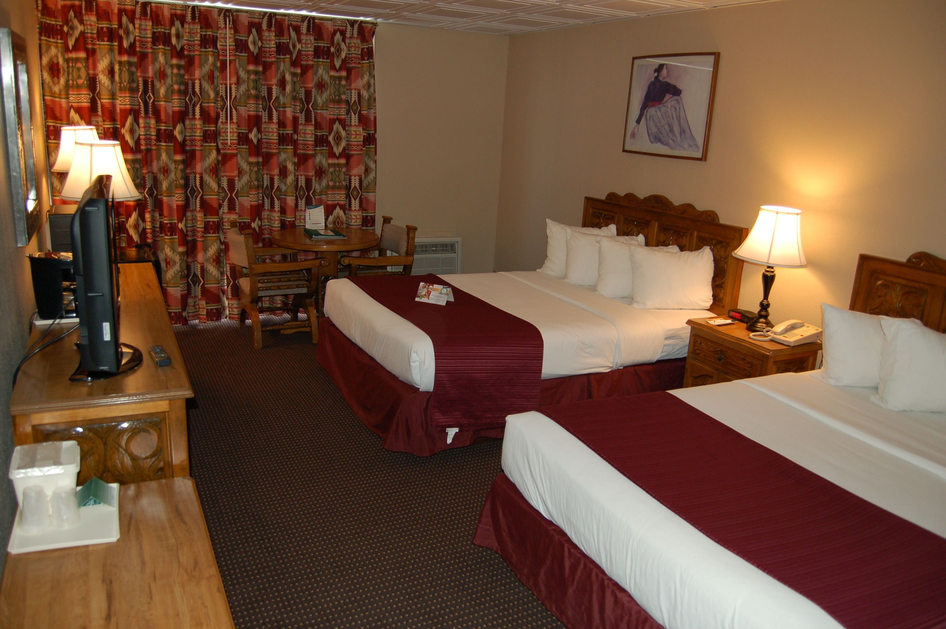 A hotel room with two beds, a desk, a chair, a lamp, a telephone, and a painting on the wall.