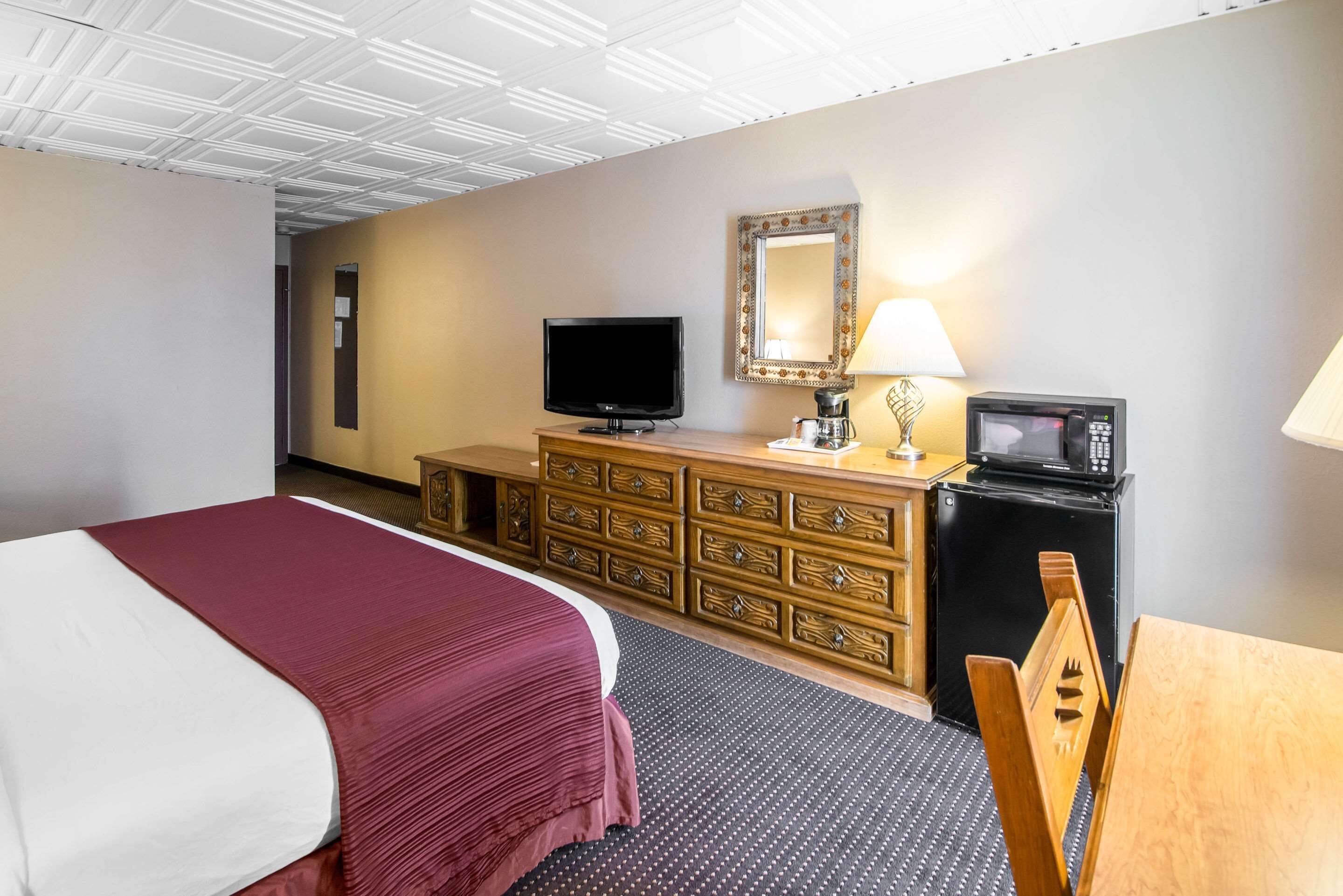 A hotel room with a large bed, a wooden dresser, a television, a microwave, and a desk with a chair.