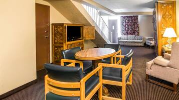 A hotel room with a round wooden table, four chairs, a sofa, and a television in a wooden cabinet.