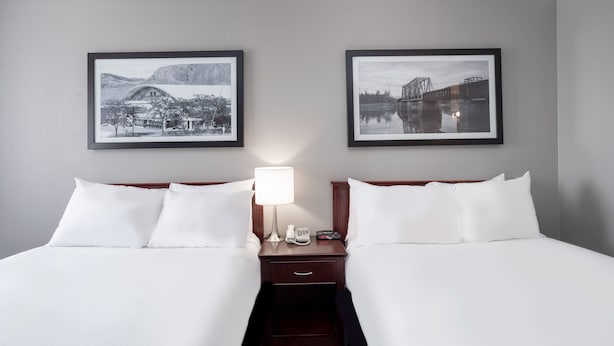 A hotel room with two beds, a nightstand with a lamp, a phone, and framed pictures on the wall. - Sandman Inn Kamloops (Kamloops)