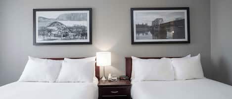 Habitación de hotel con dos camas, una mesita de noche con lámpara y dos cuadros en la pared.