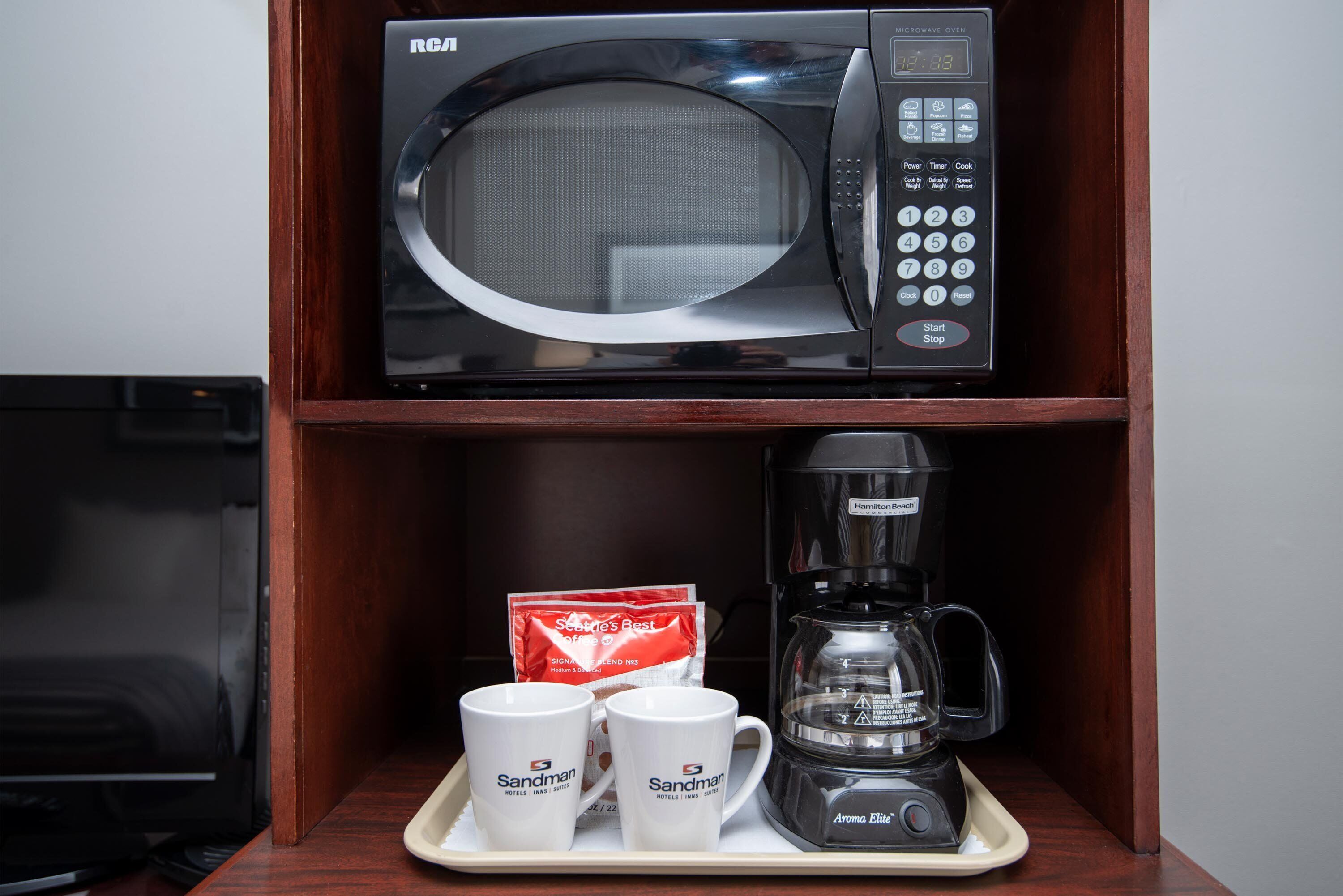 A microwave oven on a shelf, a coffee maker, and two white mugs with text on them.