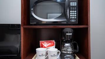 A microwave oven on a shelf, a coffee maker, and two white mugs with text on them.