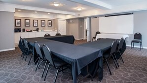 A conference room with a long table, chairs, a projector screen, and a kitchenette area. - Sandman Inn Kamloops (Kamloops)