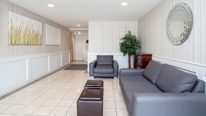 A modern living room with a grey sofa, a grey armchair, and a large mirror on the wall. - Sandman Inn Kamloops (Kamloops)