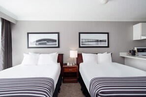 A hotel room with two beds, a nightstand with a lamp, framed pictures on the wall, and a small desk with a phone and a cup. - Sandman Inn Kamloops (Kamloops)