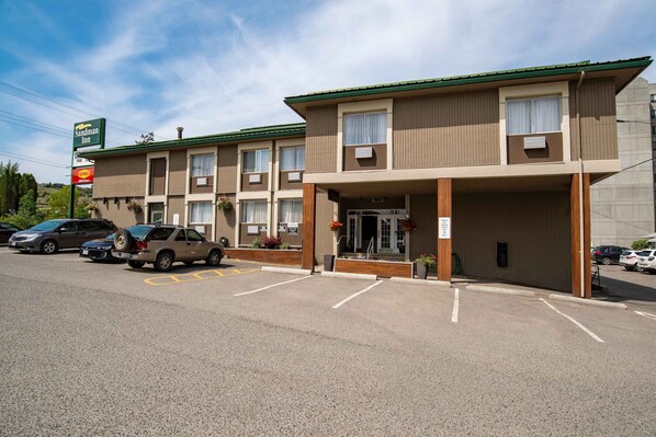 A two-story motel with a green roof and beige exterior. There are multiple parking spaces in front, and a few cars are parked.