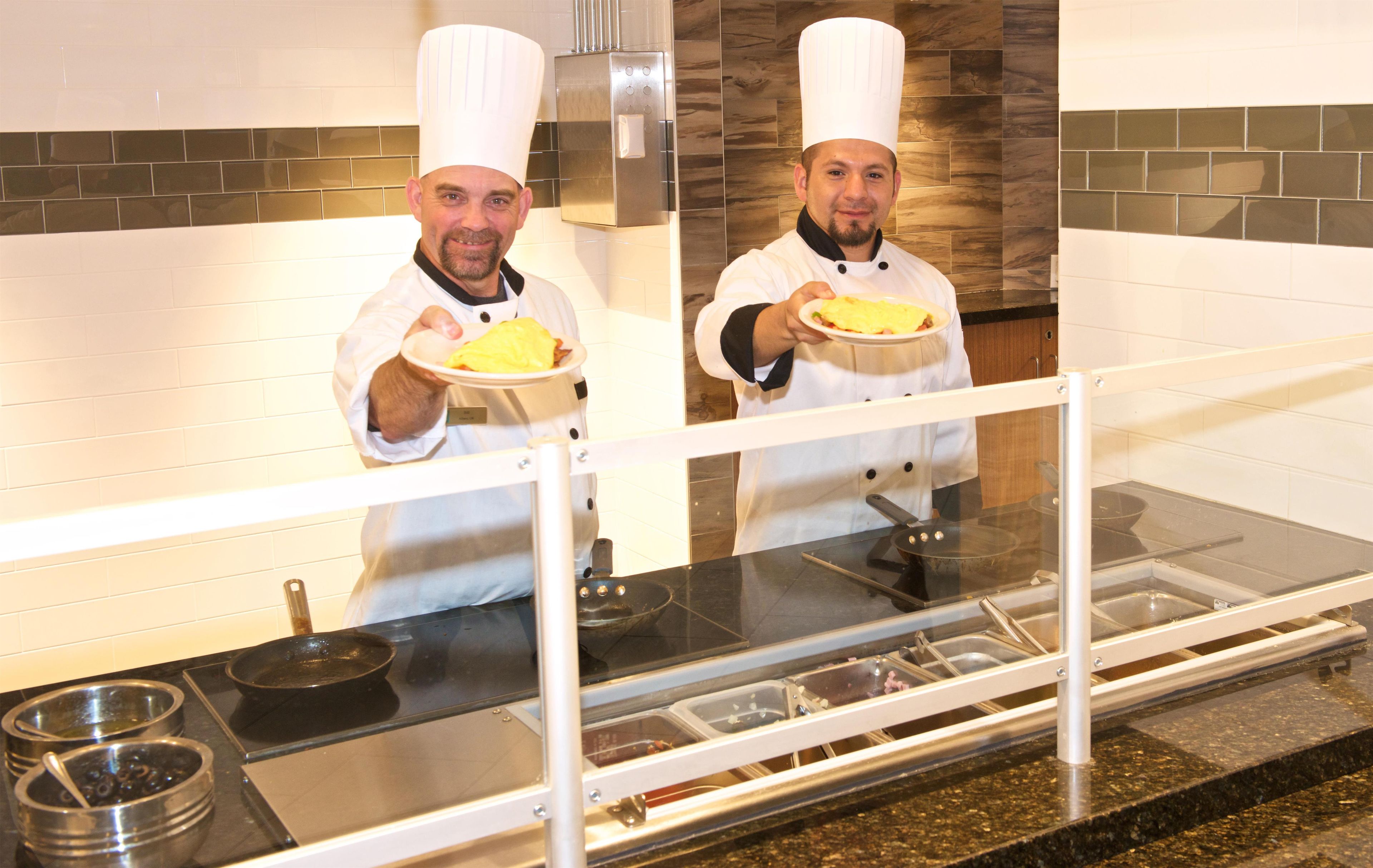 Two chefs in a kitchen holding plates of food.