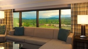 A hotel room with a large window offering a view of a green landscape and distant buildings. - Embassy Suites by Hilton Portland Tigard (Tigard)