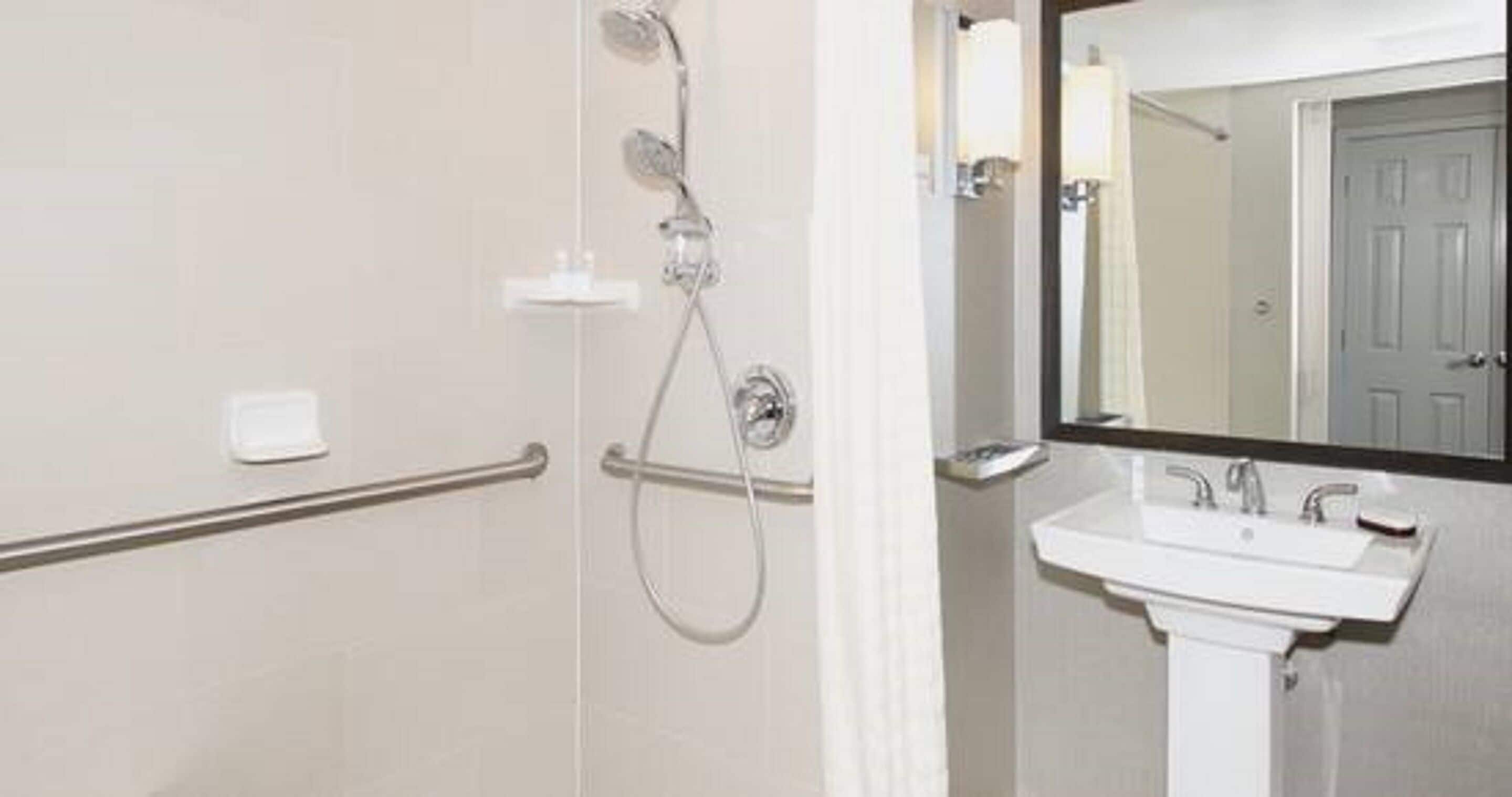 A bathroom with a shower, grab bar, and a sink with a mirror above it.