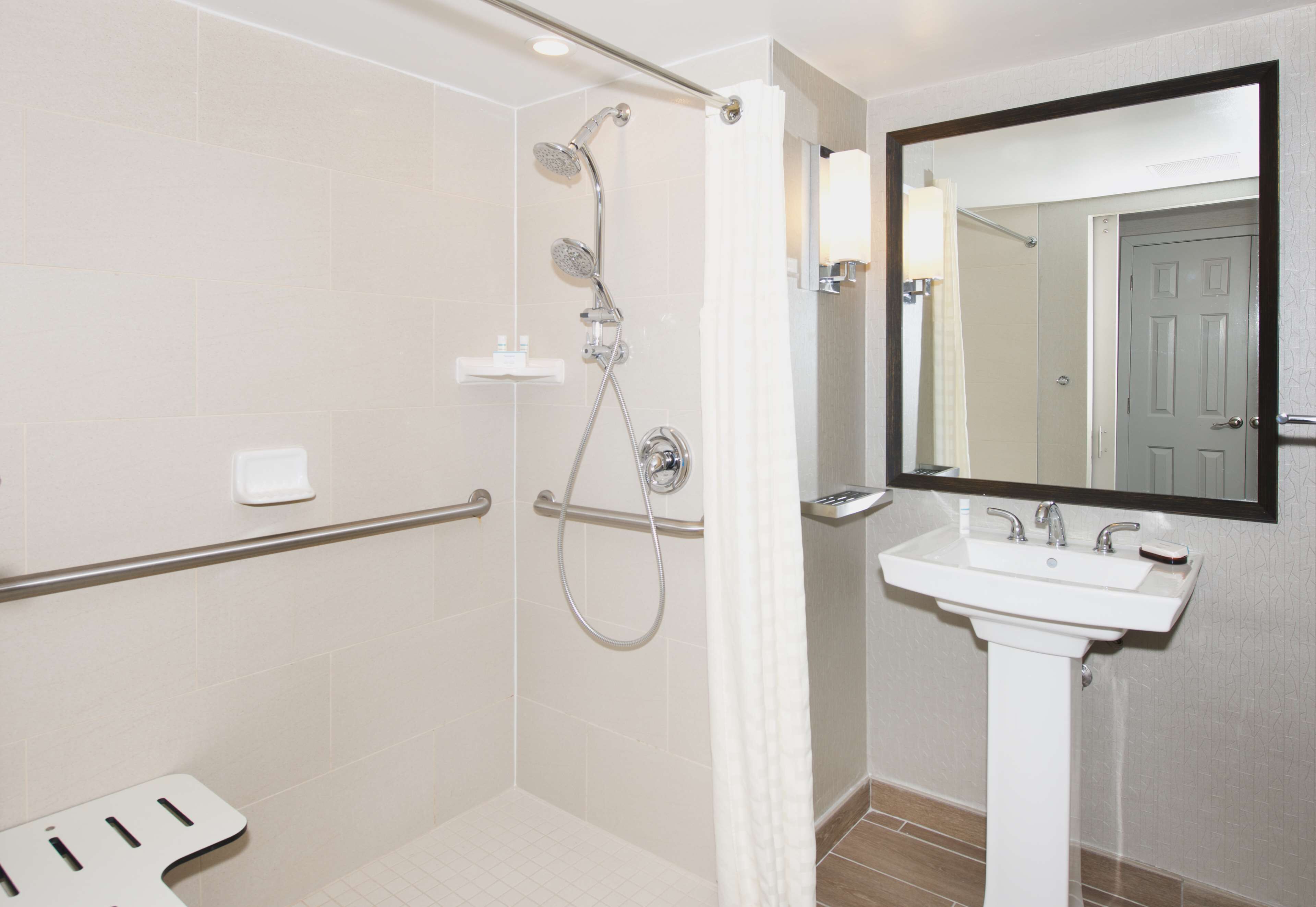 A bathroom with a shower, a sink, a mirror, and a door.