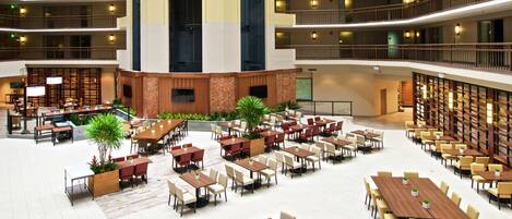 A spacious indoor dining area with multiple tables and chairs, a central seating area, and a large screen for presentations.