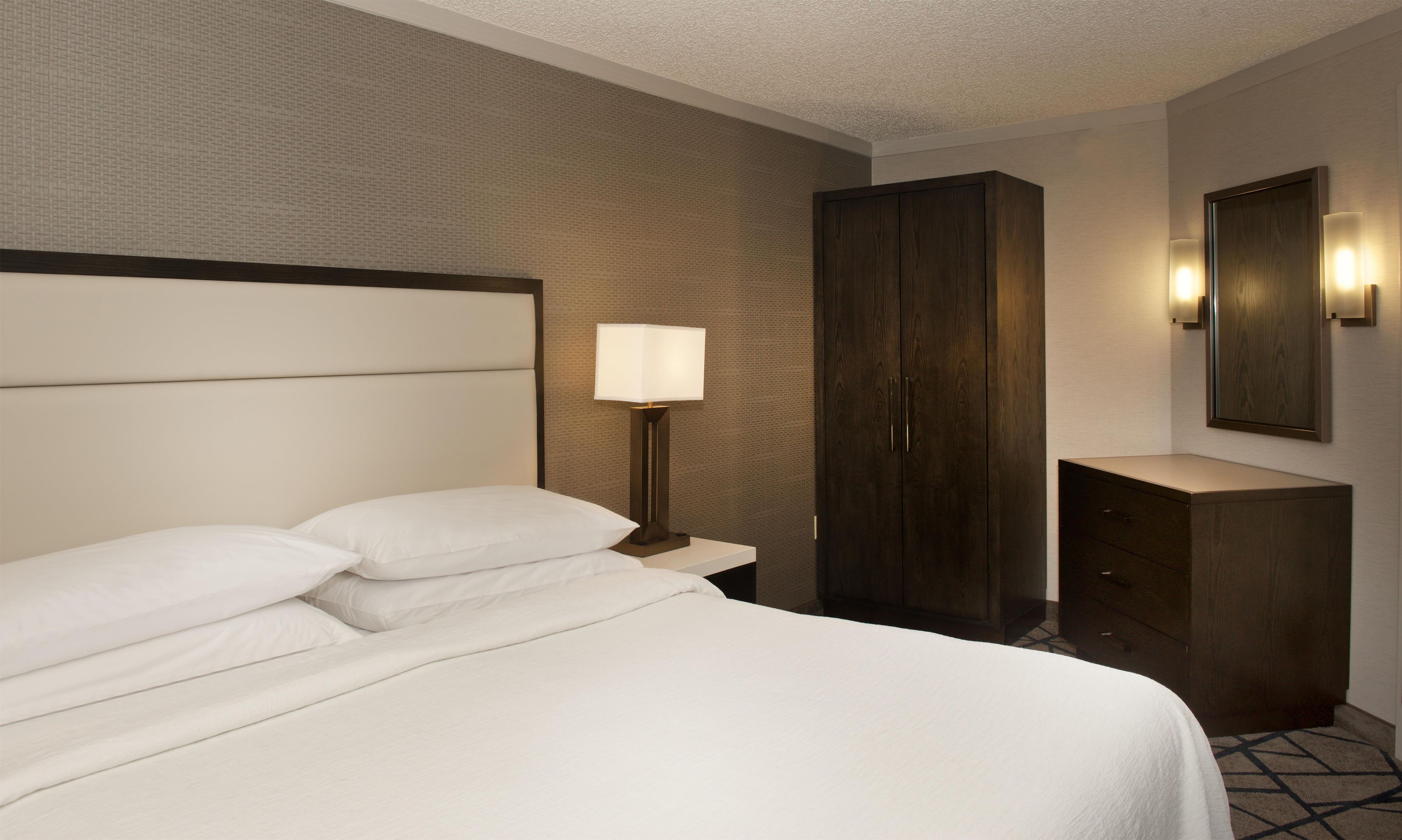 A hotel room with a bed, a nightstand, a lamp, a wardrobe, and a mirror.