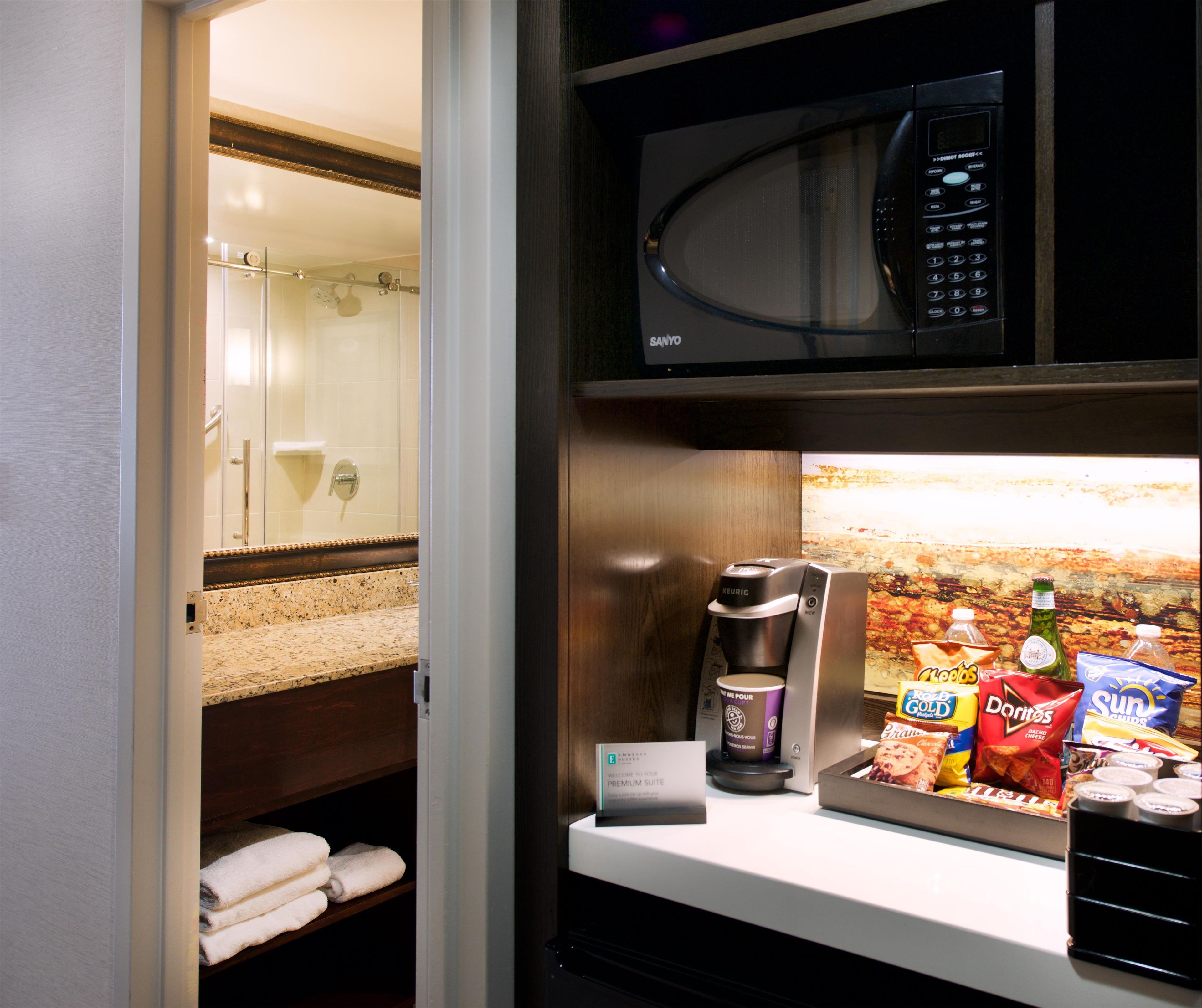 A hotel room with a shower, a microwave, a coffee maker, and snacks on the counter.