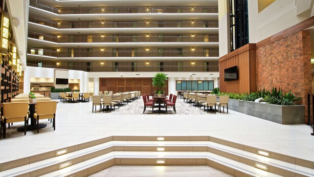 A spacious hotel lobby with multiple dining areas, a central seating area, and a staircase leading to upper floors. - Embassy Suites by Hilton Portland Tigard (Tigard)